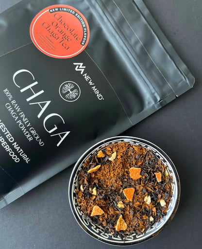 Chocolate Orange Chaga Tea leaves with dried orange pieces in a bowl next to the product bag.