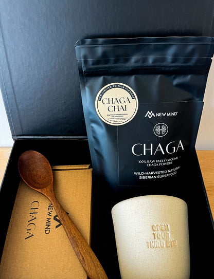 Open NEW MIND Chaga Energy Gift Box showing Chaga Chai powder bag, ceramic cup, and wooden spoon.