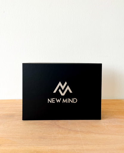 Closed black NEW MIND gift box with logo, sitting on a wooden table.