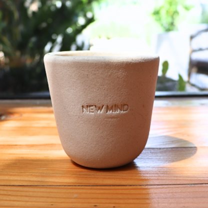 A beige hand-made ceramic intention cup placed on a wooden surface, with a plant in the background.