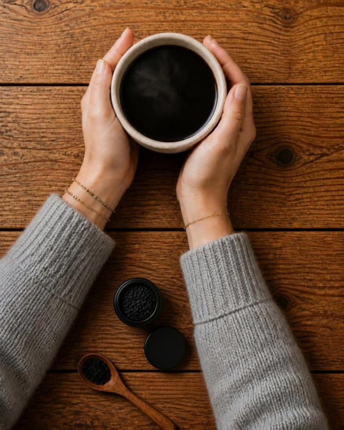 Top view of hands holding a NEW MIND ceramic cup of Crystal Black beside a small open jar of chaga crystals and a wooden spoon